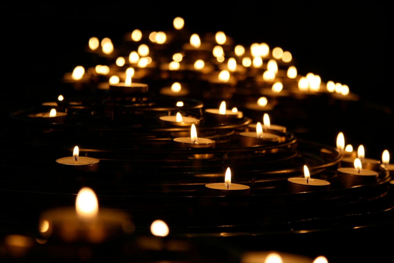 Lit tealight candles arranged in a spiral on a dark background.
