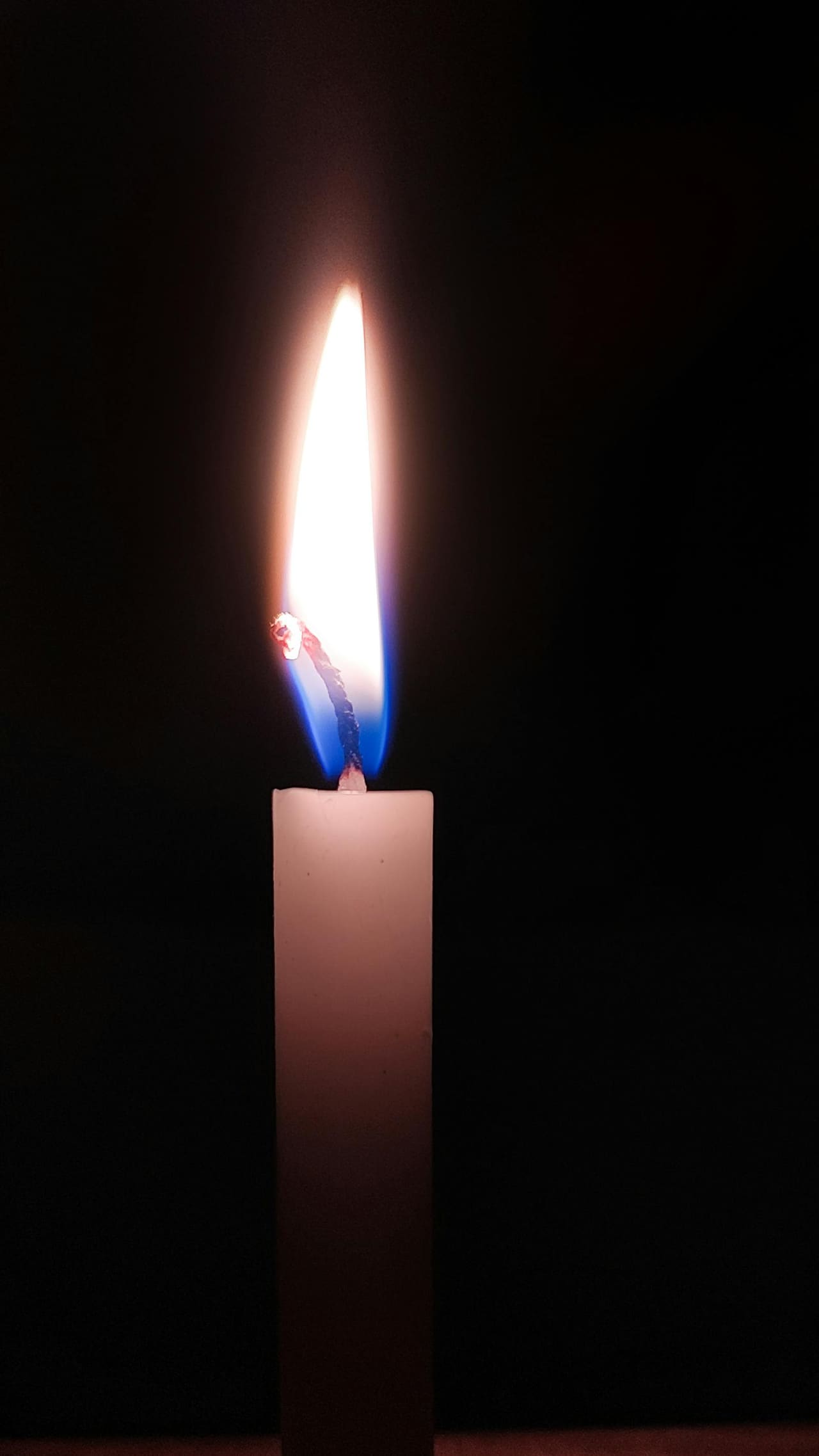 A single candle flame glowing steadily in soft darkness.